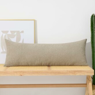 Beige long pillow on a wooden bench with a framed abstract art and a cactus nearby.