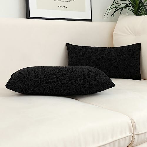 Black decorative pillows on a white sofa with a framed picture above.