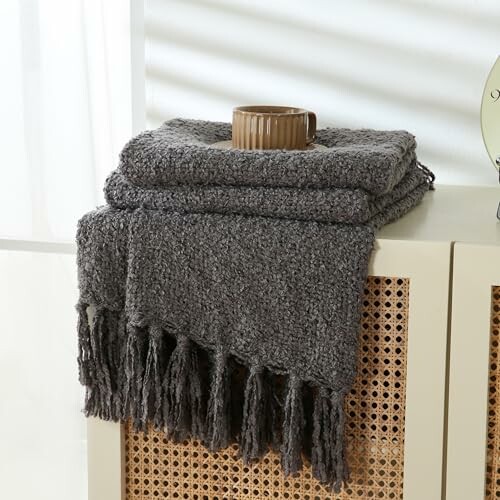 Gray blanket with fringe on a table with a cup on top