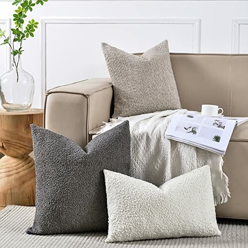 Three textured pillows on a beige sofa with a magazine and cup, next to a wooden table with a vase.