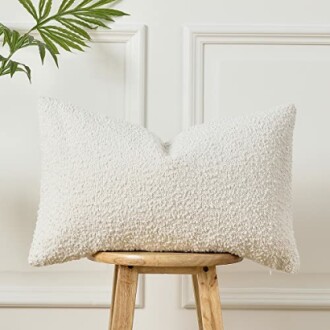 White textured pillow on a wooden stool with a leafy plant nearby.