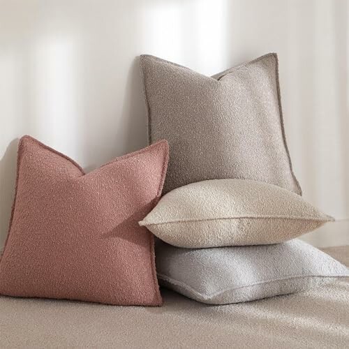 Four cozy textured pillows in neutral and pink tones stacked together.