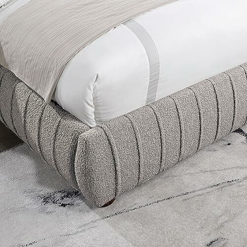 Corner of a modern upholstered bed frame with a textured gray fabric.