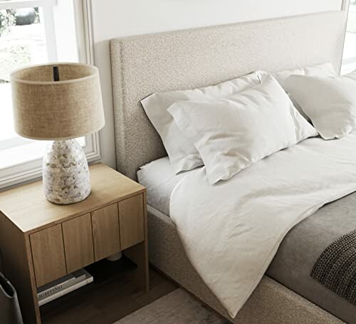 Modern bedroom with a beige bed, white bedding, and a wooden nightstand with a lamp.