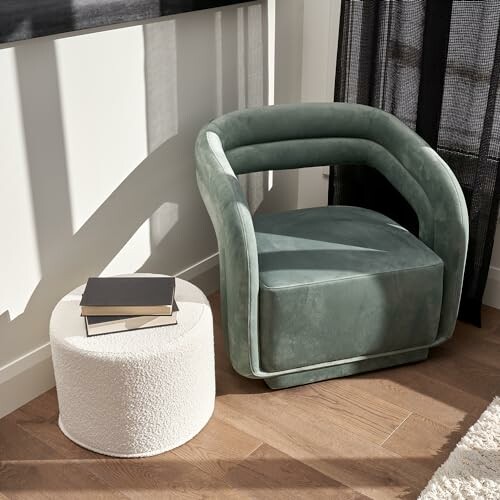 Green velvet armchair beside a round white side table with books on wooden floor.