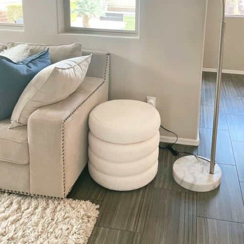 Modern living room with beige couch, round ottoman, and floor lamp, illustrating how the ottoman fits into contemporary decor.