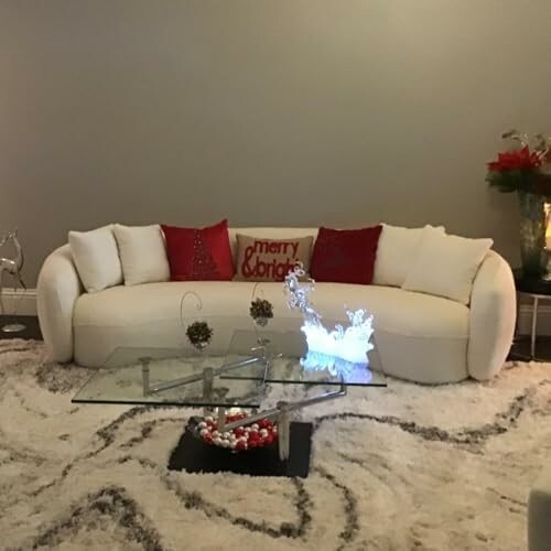 Modern living room with a white curved sofa, decorative pillows, glass coffee table, and festive decor.