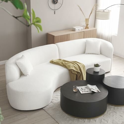 Modern living room with a white curved sofa, black coffee tables, and decor accents.