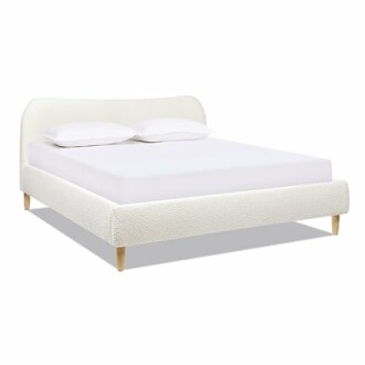 Modern upholstered bed frame with white bedding and wooden legs.