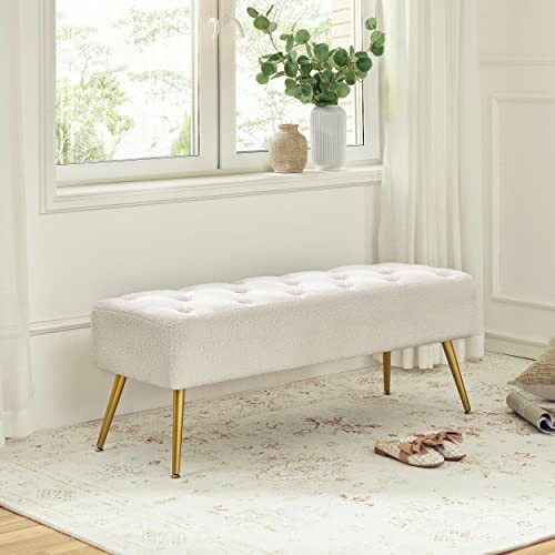 Modern upholstered bench with gold legs by a window