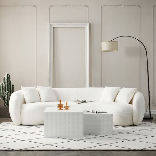 Minimalist white living room with a curved sofa, geometric coffee tables, and a floor lamp.