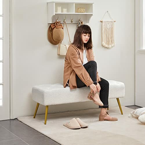 Woman sitting on a bench putting on shoes in a bedroom.